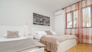 Ett sovrum med två sängar, en målning som föreställer en stadsbild, en luftkonditioneringsanläggning och tunna, genomskinliga gardiner.