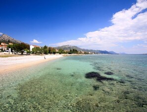 Une plage avec une eau claire et peu profonde, un rivage sablonneux et des bâtiments le long de la côte.