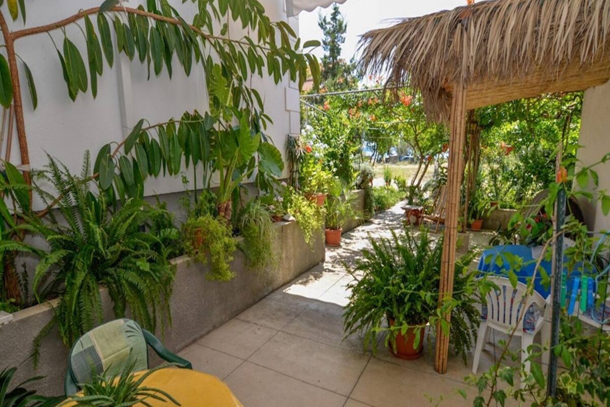 A covered outdoor area with potted plants, a yellow table, and a thatched roof structure.