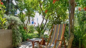 Ein Holzstuhl mit gestreifter Sitzfläche, ein kleiner Tisch und Blumentöpfe in einer schattigen Außenbereich.