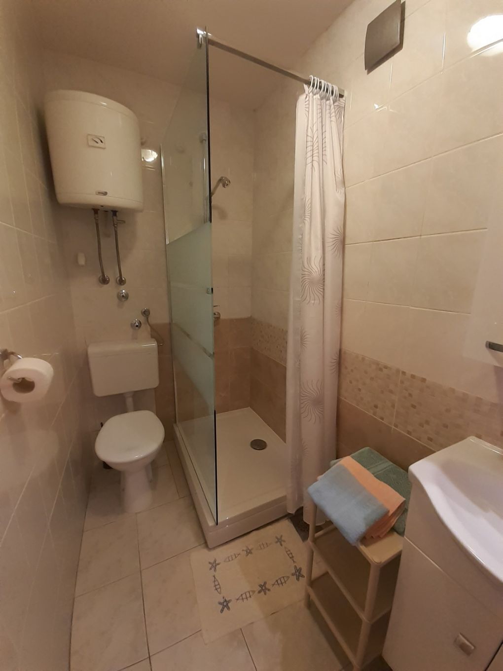 Un baño con ducha de vidrio, inodoro, lavamanos y toallero.