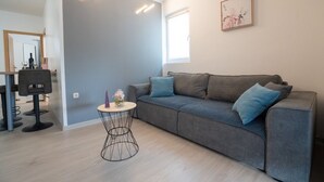 A modern living room with a grey sofa, a small round table, and a dining area with chairs. - Apartment Danka (Novalja)