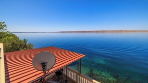 A balcony with a red roof overlooking a calm lake with clear water and a distant shoreline. - Apartment Dalibor (Karlobag)