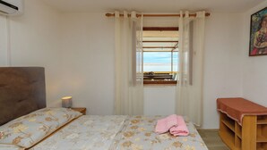 A bedroom with a bed, a bedside lamp, a window with curtains, a wooden bench, and a painting on the wall. - Apartment Dalibor (Karlobag)