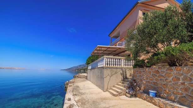 A coastal building with a stone wall, a balcony, and a clear view of the sea. - Apartment Dalibor (Karlobag)