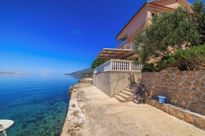 Un edificio costero con muro de piedra, balcón y vista despejada al mar.