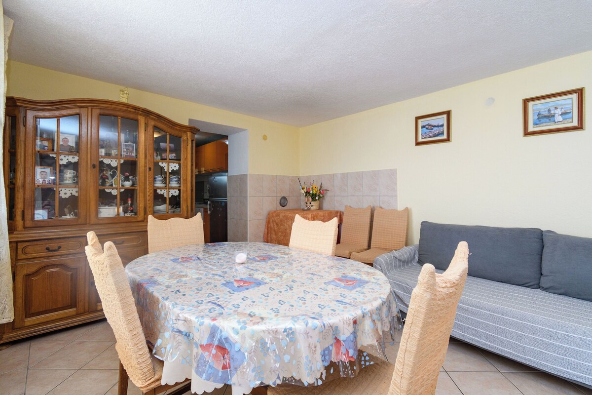 Ein Essbereich mit rundem Tisch, Stühlen, einer Schrank mit Glastüren, einer Couch und zwei gerahmten Bildern an der Wand.
