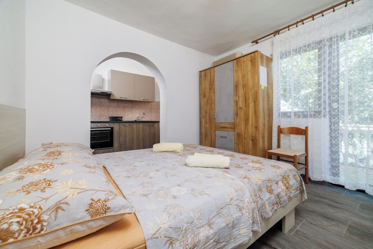 Ein Schlafzimmer mit einem großen Bett, einem Holzschrank, einem Holzstuhl und Blick auf eine Küche durch einen Bogen.