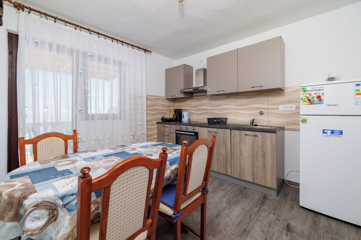 Eine kleine Küche mit Holzschränken, einem Kühlschrank und einem Esstisch mit Stühlen.