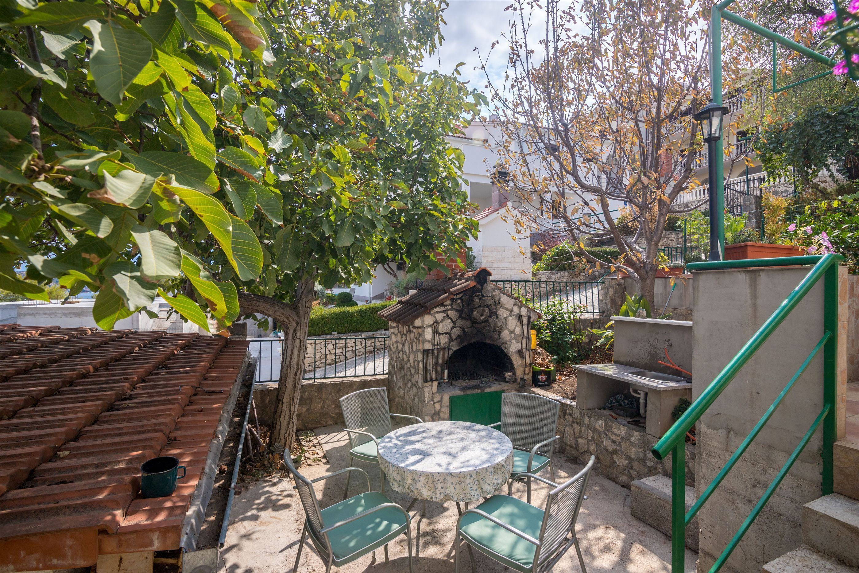 An outdoor patio with a stone fireplace, green chairs, and a tiled roof.