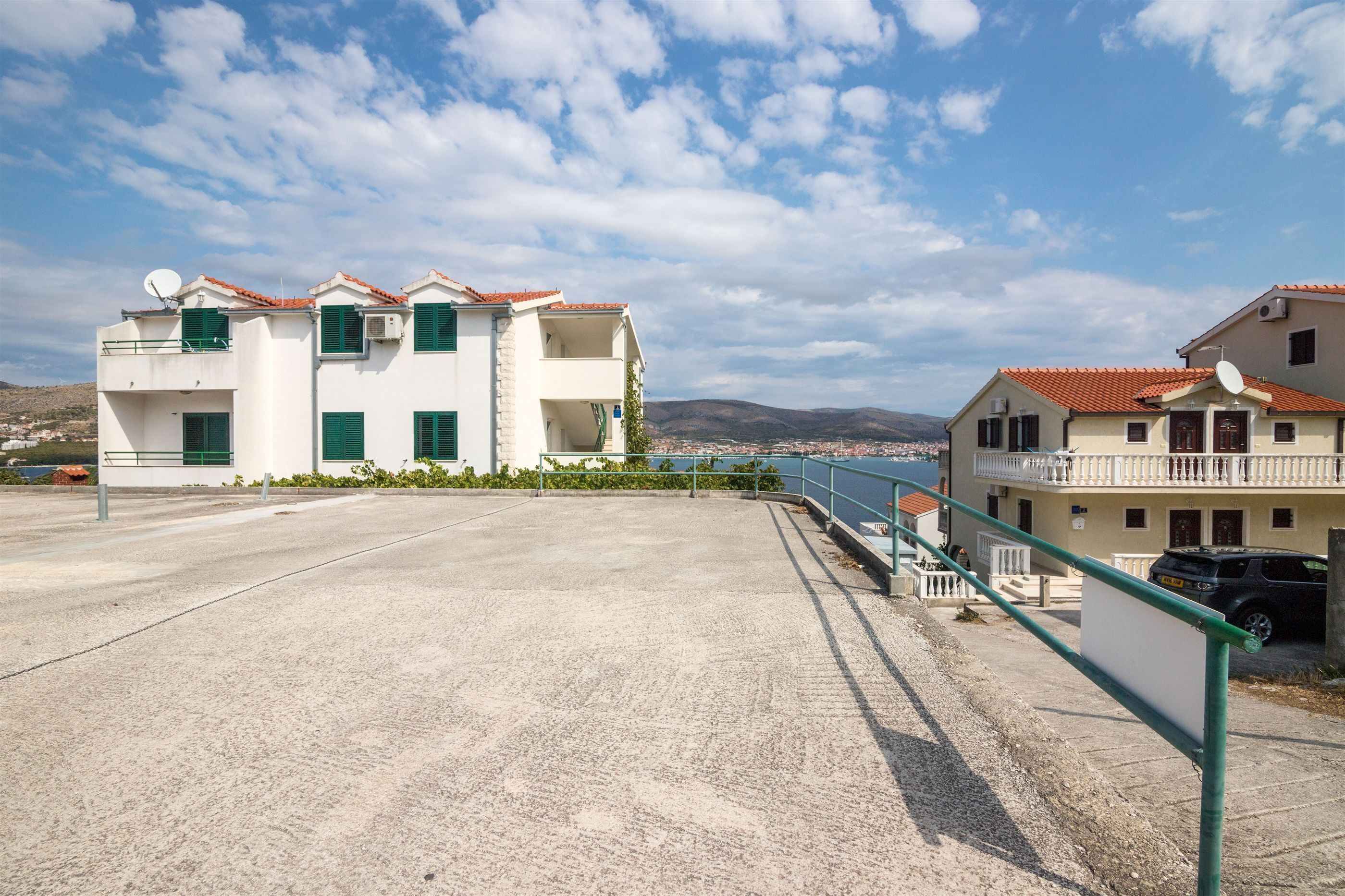 Uma área residencial costeira com edifícios brancos, persianas verdes e vista clara para o mar.