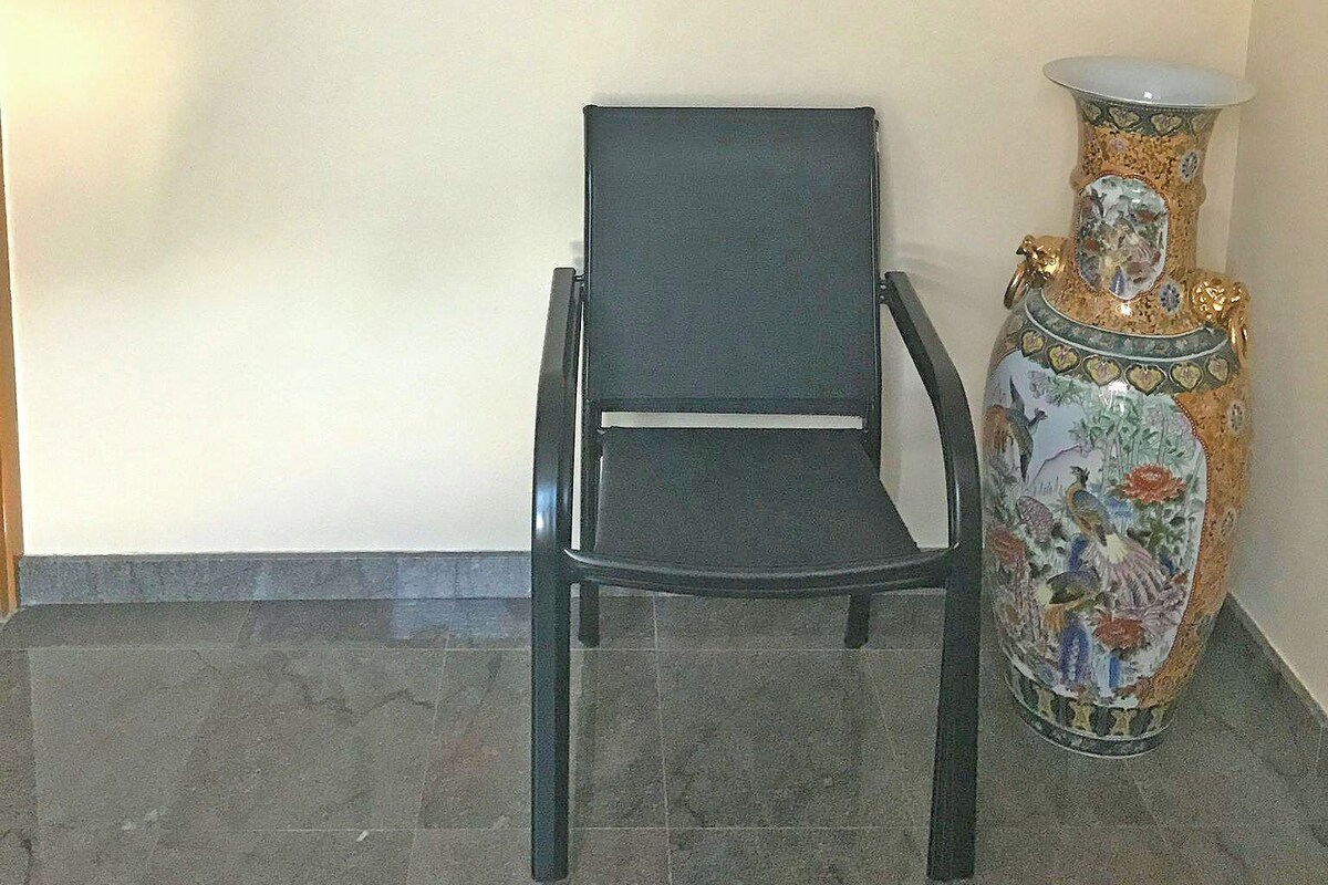 A chair and a decorative vase against a plain wall.