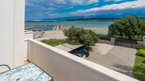 A balcony with a view of a marina, a paved area with a car, and a tree. - Apartments Blue Skies (Razanac)