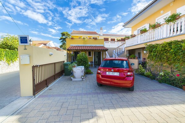 A red car parked in a driveway with a yellow building in the background. - Apartments Nadica (Nin)