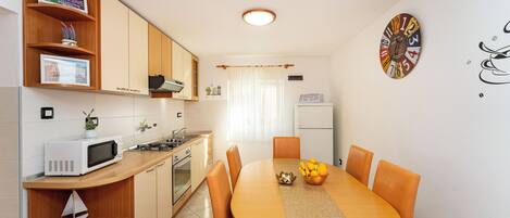 A compact kitchen with wooden cabinets, a microwave, a stove, and a dining table with orange chairs.