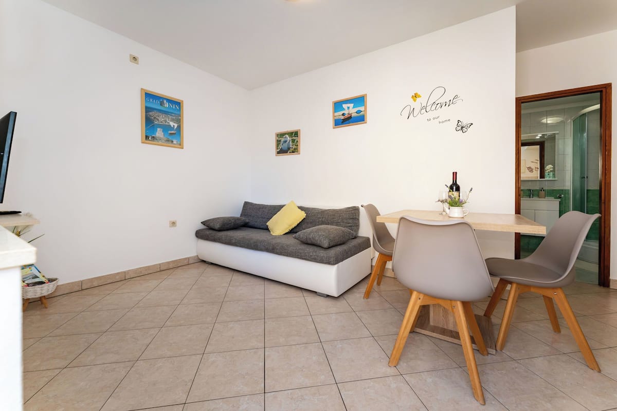 Ein modernes Wohnzimmer mit Sofa, Esstisch und Stühlen. An den Wänden sind Dekorationen und ein Fernseher angebracht.