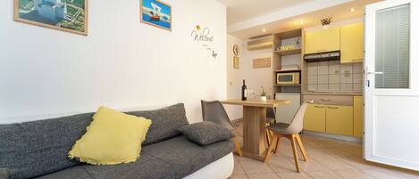 A modern living room with a grey sofa, a yellow throw pillow, and a dining area with a wooden table and chairs.