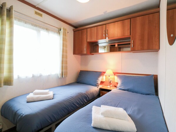 A small, cozy room with two beds, wooden cabinets above, and a window with curtains. - No 35 MP Billing Aquadrome Holiday Park (Northampton)