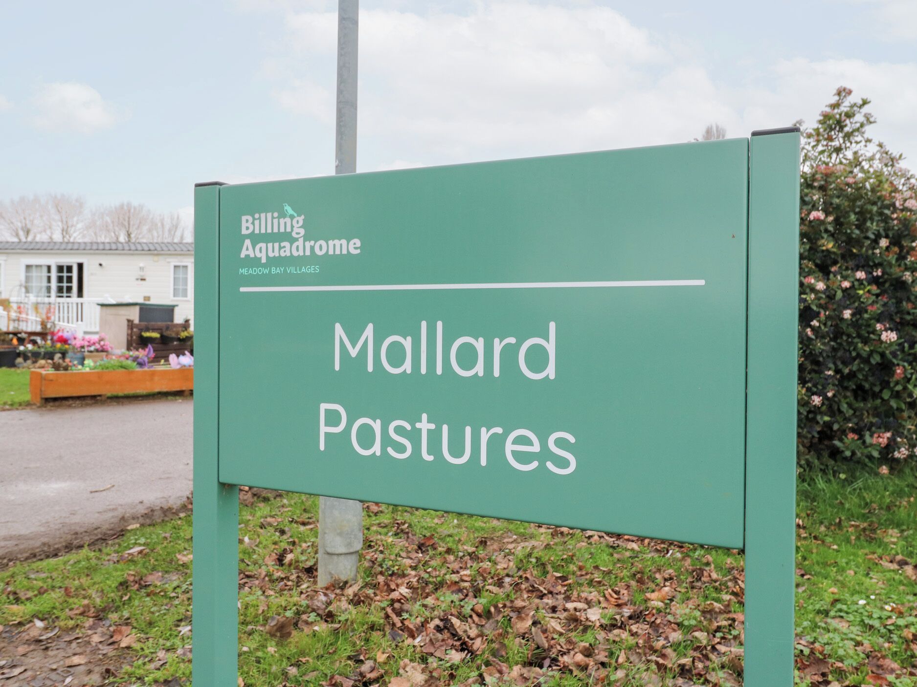A sign for Mallard Pastures, part of Meadow Bay Villages, with a green background and white lettering.