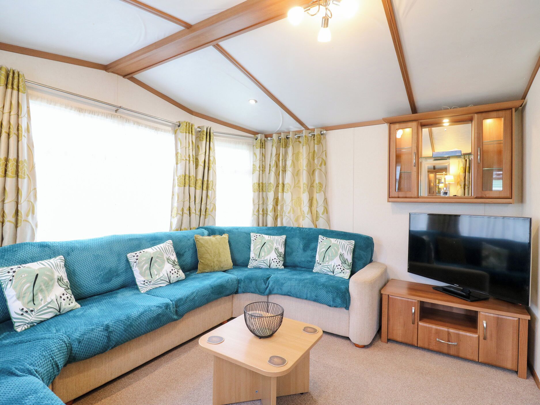 A living room with a sectional sofa, a flat-screen TV, wooden cabinets, and a ceiling with exposed beams.