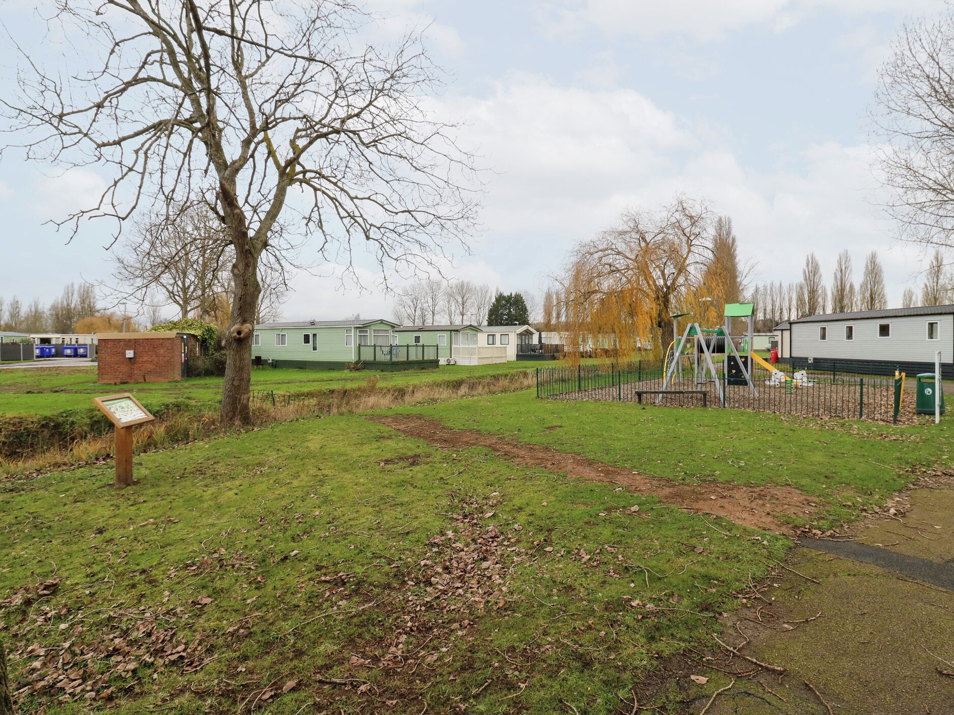 A park with a playground, a grassy area, and a row of mobile homes in the background.