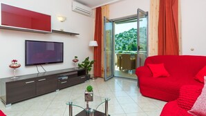 A modern living room with a red sofa, a flat-screen TV, a dark wooden cabinet, and a glass coffee table. - House Silva (Rogoznica)