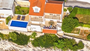 An aerial view of a coastal property with a swimming pool, multiple balconies, and a rocky shoreline. - House Silva (Rogoznica)