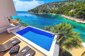 Ein Pool mit Blick auf ein türkisfarbenes Meer und eine gebirgige Landschaft.