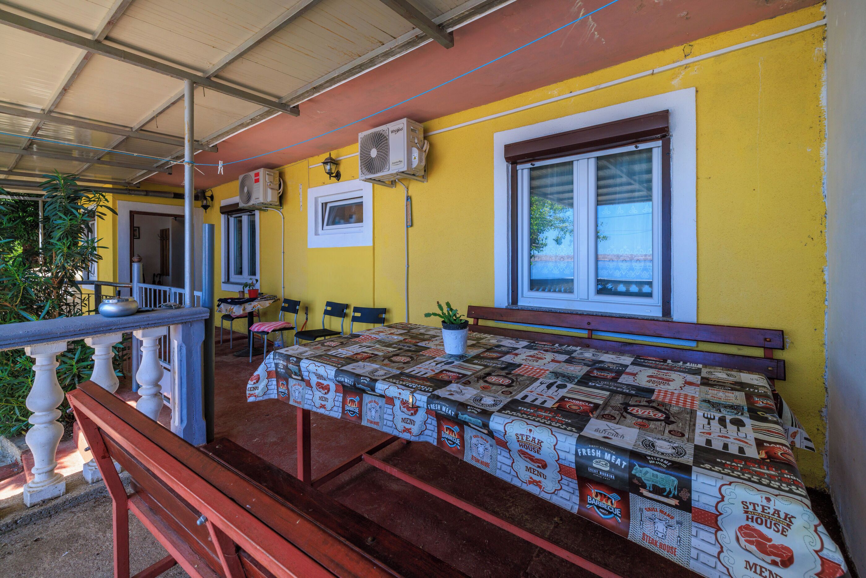 Ein Restaurant mit gelber Fassade, einer überdachten Außenbereich-Sitzgelegenheit und einem Tisch mit Tischdecke im Stil eines Steakhauses.