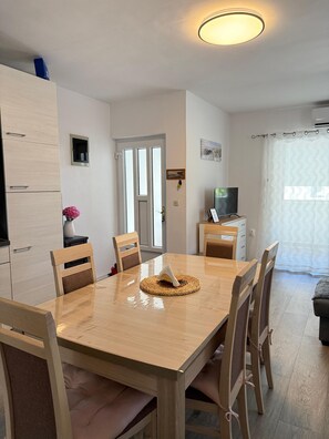 A dining area with a wooden table, chairs, and a ceiling light fixture. - Apartment Kety (Novalja)
