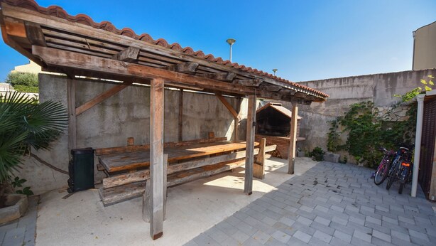 A wooden pergola with a tiled roof, a brick barbecue area, and a paved patio with bicycles. - Apartment Kety (Novalja)