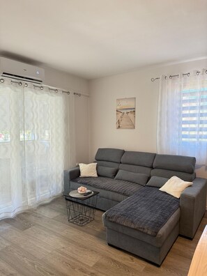 A modern living room with a grey sectional sofa, a small round coffee table, and a wooden floor. - Apartment Kety (Novalja)