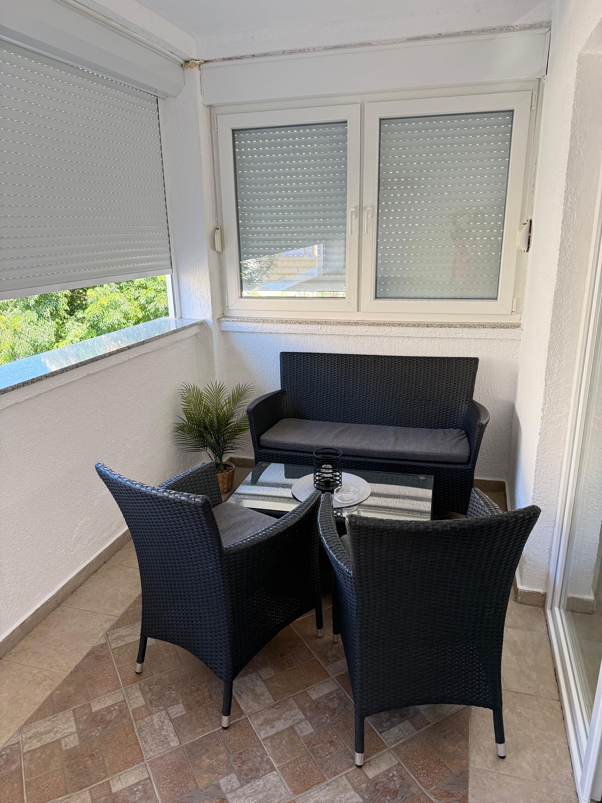 A balcony with a wicker sofa, two chairs, a small table, and a potted plant.
