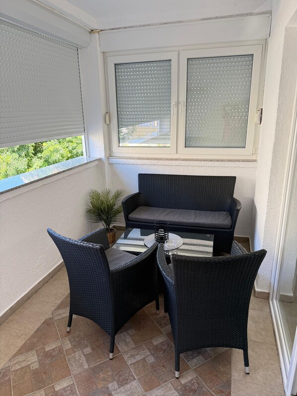 En balkong med en soffa av rotting, två stolar, ett litet bord och en krukväxt.