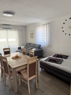 A modern living space with a dining area, sofa, and a wall clock. - Apartment Kety (Novalja)