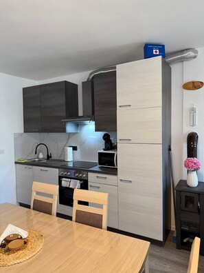 A compact kitchen with dark cabinets, a microwave, a stove, and a sink. - Apartment Kety (Novalja)