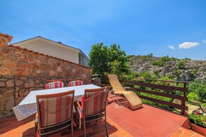 A patio with a table and chairs, a stone wall, and a wooden fence overlooking a mountainous landscape. - Apartment Ivan (Karlobag)