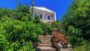 A building with a balcony, surrounded by lush greenery and a stone staircase leading up to it. - Apartment Ivan (Karlobag)