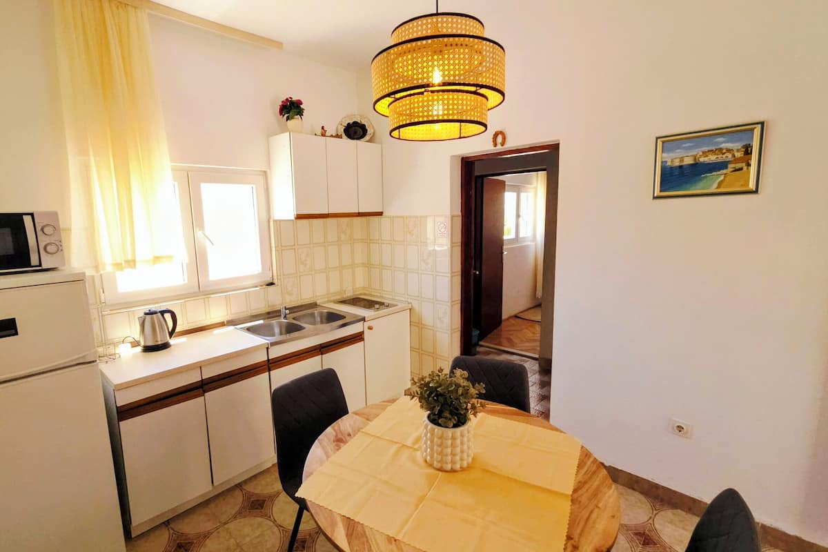 A compact kitchen with a microwave, kettle, sink, and a dining table with chairs.