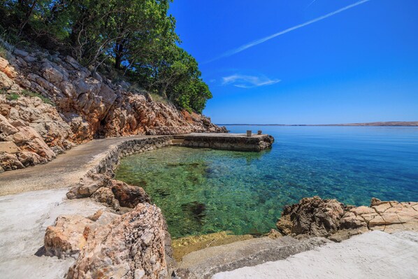 A clear coastal path leading to a calm sea, surrounded by rocky terrain and dense greenery. - Apartments Jase (Karlobag)