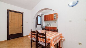 A dining area with a table covered in a checkered tablecloth, wooden chairs, and a kitchen in the background. - Apartments Jase (Karlobag)