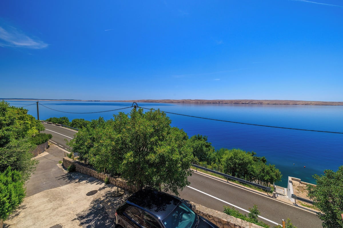 A coastal road with a parked car, a stone wall, and a clear view of the sea.