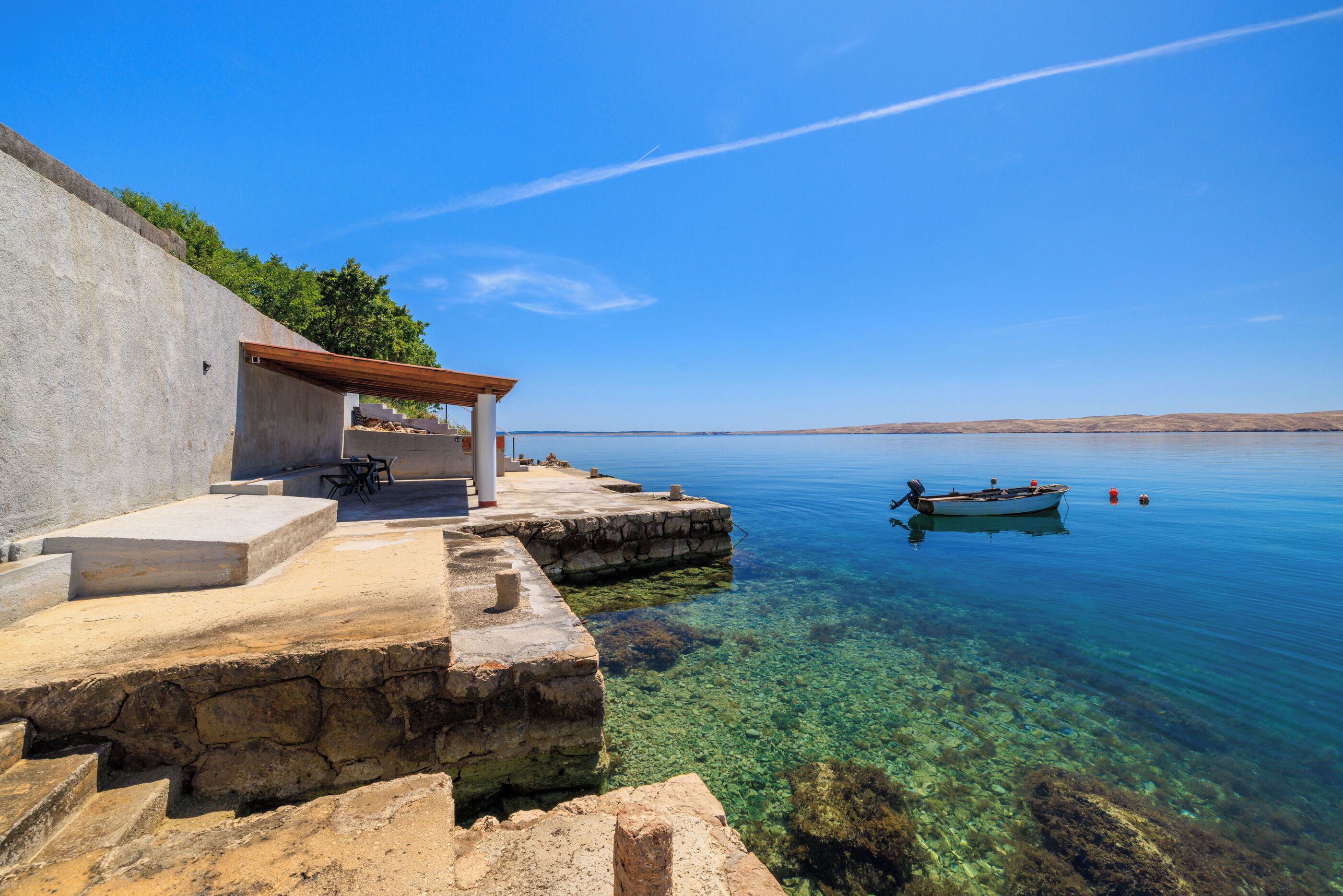 A stone staircase leading to a covered area by a calm lake with a boat anchored nearby.