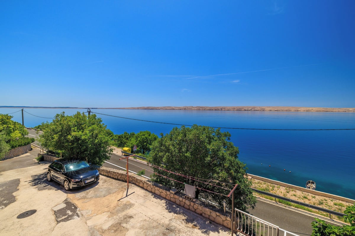 A coastal road with a parked car, a stone wall, and a view of the sea.