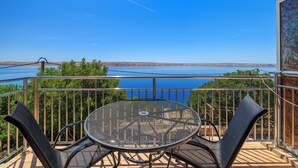 A balcony with a round metal table and four chairs, overlooking a body of water and distant land. - Apartments Jase (Karlobag)