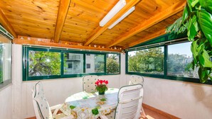 Una veranda riparata con tavolo e sedie, ampie finestre e una ventola a soffitto.