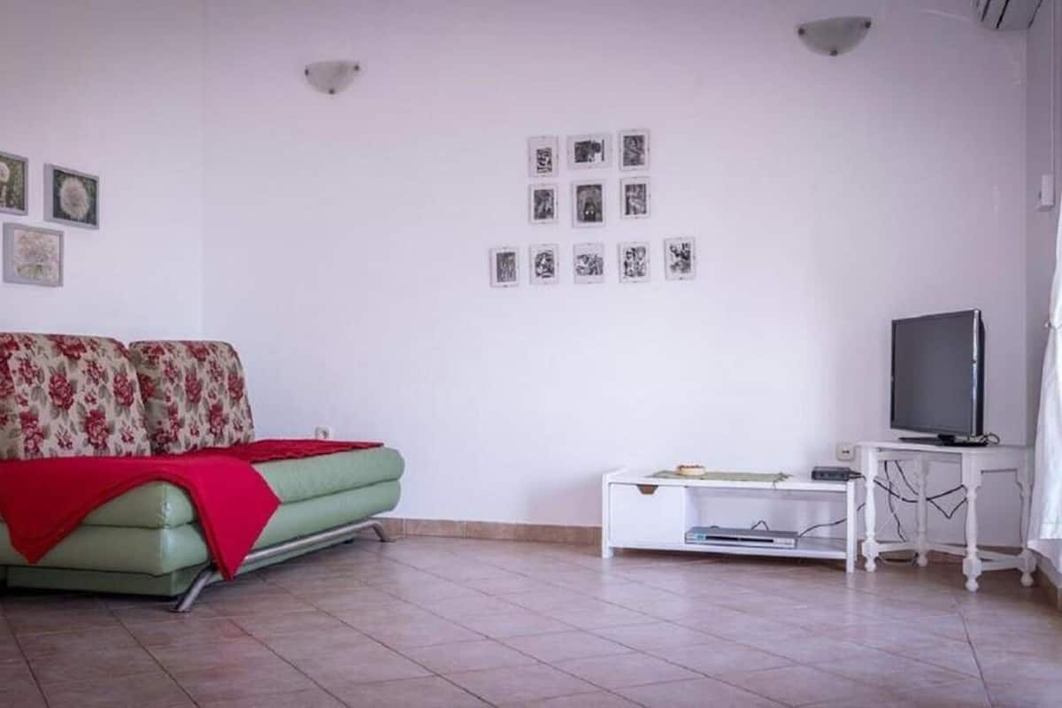 A living room with a green sofa, a white TV stand, and a wall with framed pictures.
