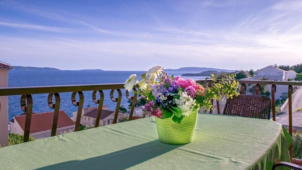 Un balcón con una mesa, una silla de mimbre y un florero con flores.