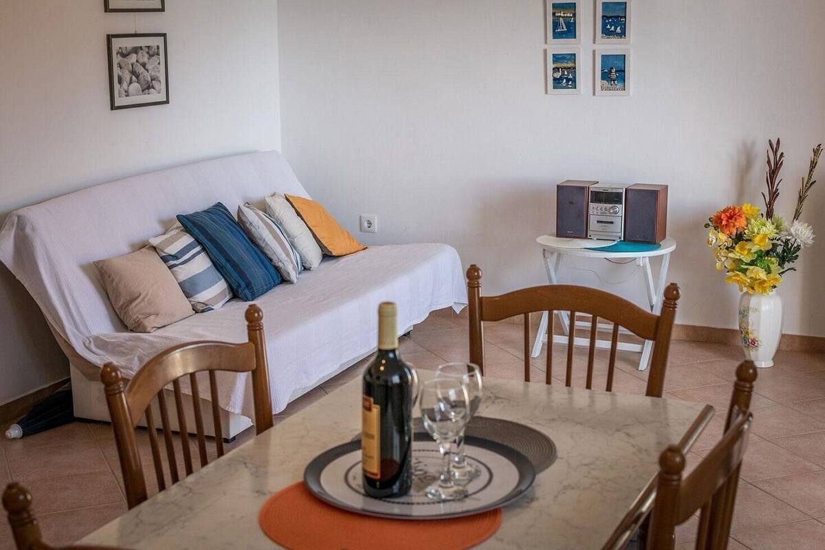 A dining area with a table set for two, a bottle of wine, and a vase of flowers.
