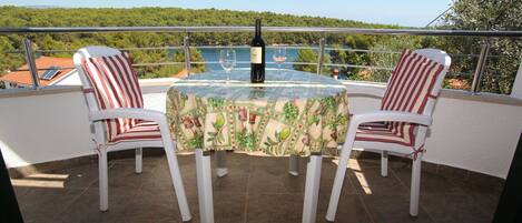 A balcony with a table set for two, featuring a bottle of wine and two glasses.